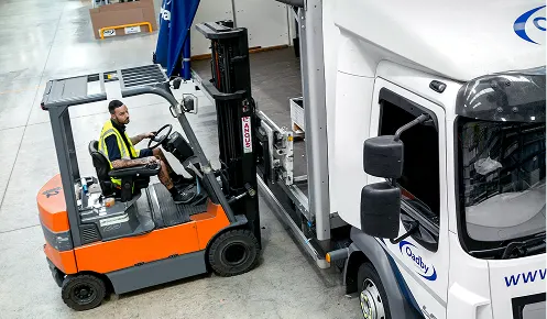 A forklift truck loading a pallet onto an Oadby Plastics truck in the warehouse loading bay