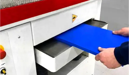 Operator feeding a piece of engineering plastic into a planing machine at Oadby Plastics