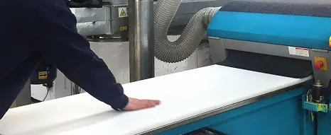 An operator feeding in a sheet of semi-finished plastic sheet into a planing machine at Oadby Plastics