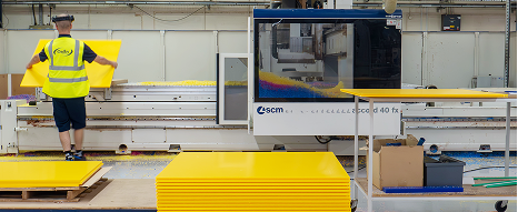 Operators at a CNC machine placing a large sheet of yellow plastic at Oadby Plastics