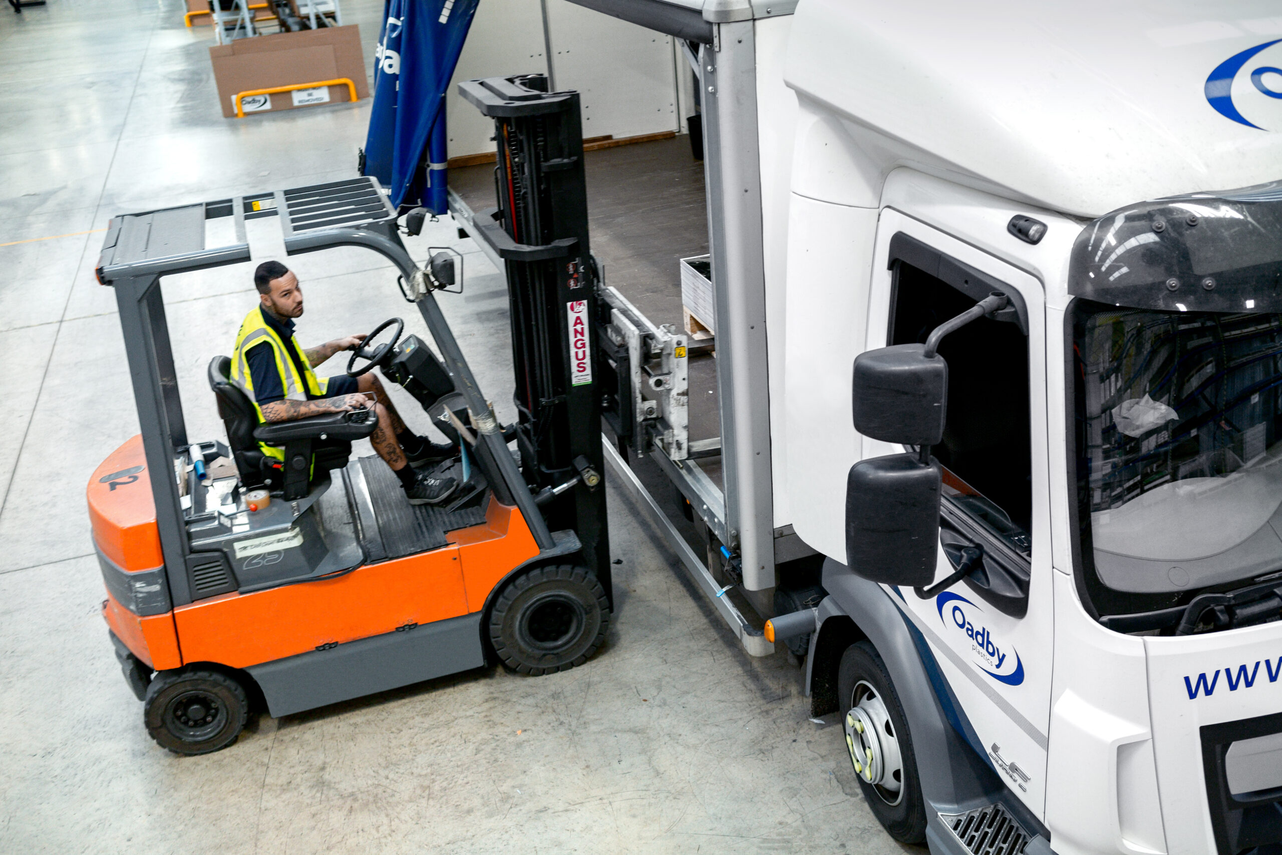 A forklift truck loading a pallet of precisely machined CNC plastic parts onto an Oadby Plastics branded truck, delivering from its large warehouse across the UK with next-day delivery options available.